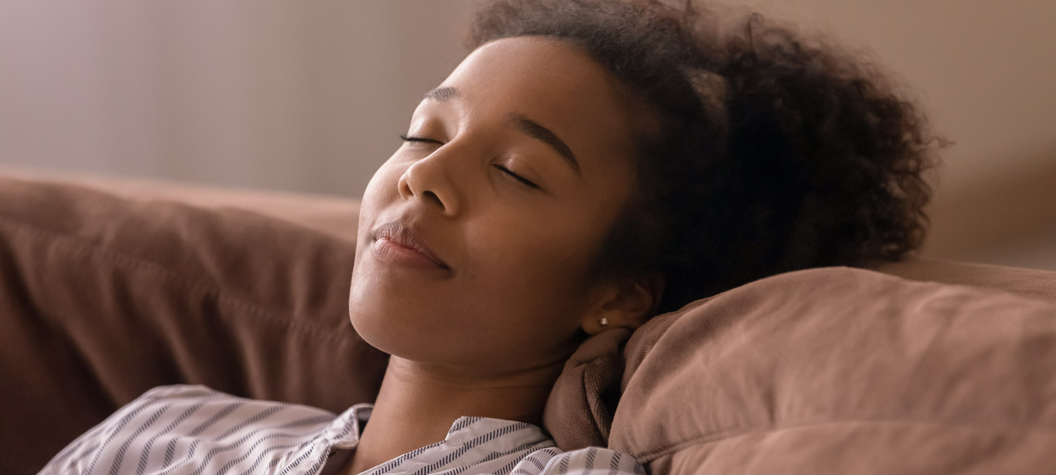 Relaxed young African American woman, peaceful teen girl resting on soft couch at home, sleeping with serene face, breathing fresh cool conditioned air, enjoying relaxation, break. Close up